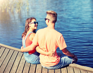 holidays, vacation, love and people concept - happy teenage couple sitting and hugging on river berth at summer