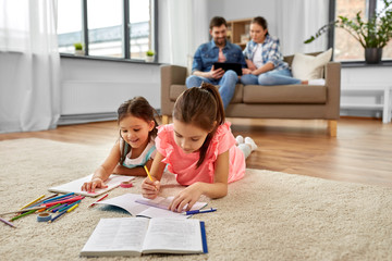 family, leisure and childhood concept - happy sisters lying on floor and drawing and doing homework...