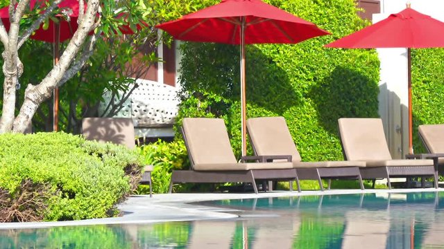 Deck chairs wait for tourists alongside a luxury hotel resort swimming pool.