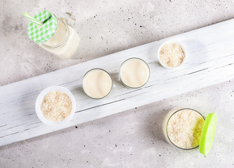 Set of glass containers with healthy rice milk and rise seeds on diagonal wooden board on concrete background. 