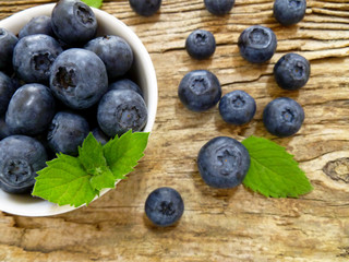 Bowl of fresh blueberries on rustic wooden old table. Freshly picked blueberries in bowl. Healthy organic fruit background. Organic food raw blueberries and mint leaf for healthy lifestyle.