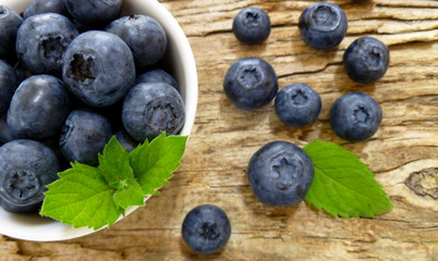 Bowl of fresh blueberries on rustic wooden old table. Freshly picked blueberries in bowl. Healthy organic fruit background. Organic food raw blueberries and mint leaf for healthy lifestyle.