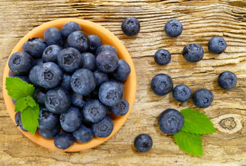 Bowl of fresh blueberries on rustic wooden old table. Freshly picked blueberries in bowl. Healthy organic fruit background. Organic food raw blueberries and mint leaf for healthy lifestyle.