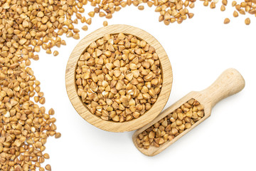 Lot of whole raw brown buckwheat grain in a wooden bowl with wooden scoop flatlay isolated on white background