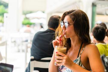 Portrait of young woman at the restaurant drinking frappe coffee in a summer day on the vacation wearing sunglasses