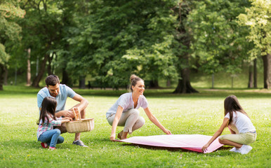 family, leisure and people concept - happy mother with daughter laying down picnic blanket on grass in summer park