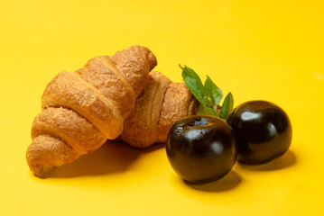 French croissants and fresh plums on yellow background close up. Summertime meal	