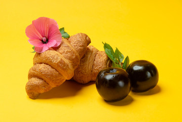 French croissants and fresh plums on yellow background close up. Summertime meal	