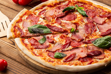 Pizza with ham , hot sausages, salami and mozzarella on wooden background close up. Italian cuisine. Pizza with prosciutto and salami on wooden table. top view.