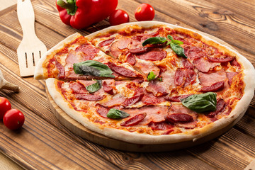 Obraz na płótnie Canvas Pizza with ham , hot sausages, salami and mozzarella on wooden background close up. Italian cuisine. Pizza with prosciutto and salami on wooden table. top view.