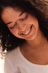 Portrait of young pretty smiling woman with dark curly hair laughing and happily closing eyes isolated