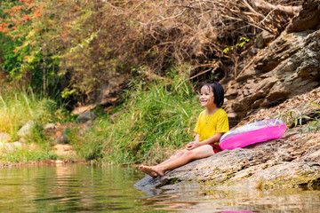Little Asian female kid sitting on rock aside the river with pink pool ring