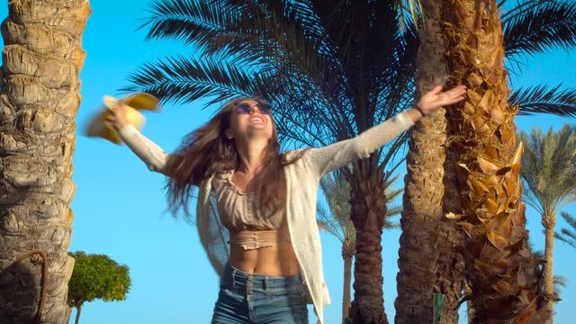 Happy young woman jumping, playing with hat and having fun under palm trees in Egypt. Summer vacation