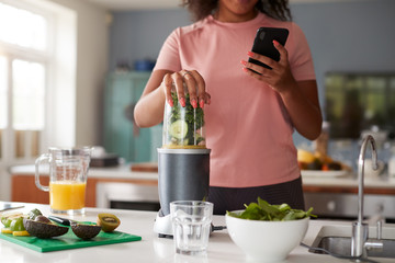 Close Up Of Woman Using Fitness Tracker To Count Calories For Post Workout Juice Drink She Is Making - obrazy, fototapety, plakaty
