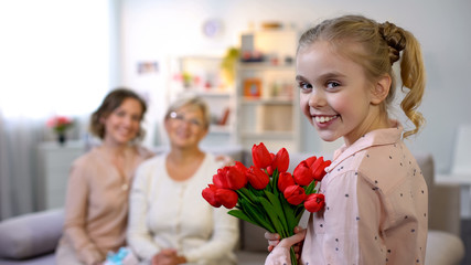 Old mother and daughter looking at small girl giving tulips, smiling at camera