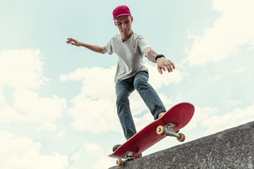 Skateboarder doing a trick at the city's street in sunny day. Young man in sneakers and cap riding...