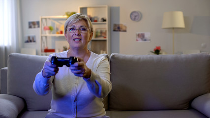 Happy mature lady playing video game on console, sitting home on sofa, leisure