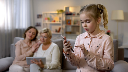 Obraz premium Pretty child using smartphone app, grandmother and mother scrolling tablet