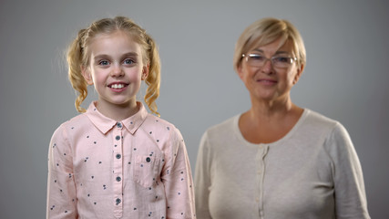 Adorable little girl smiling at camera, senior lady standing behind, support