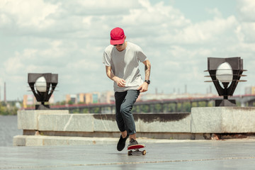 Skateboarder doing a trick at the city's street in sunny day. Young man in sneakers and cap riding...
