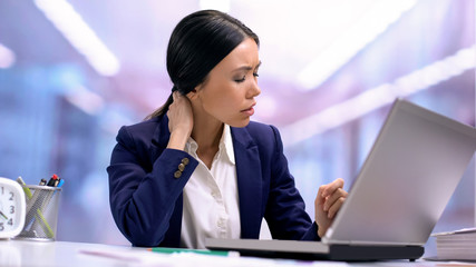 Tired business woman suffering from neck pain sitting front laptop, health care