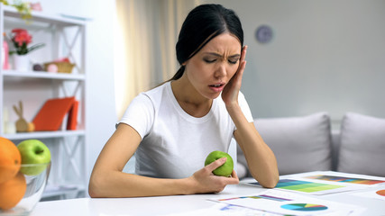 Young female freelancer suffering toothache holding green apple, inflammation