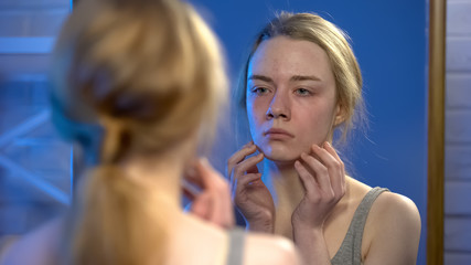 Unhappy young lady looking in mirror reflection, skin imperfection, insecurity
