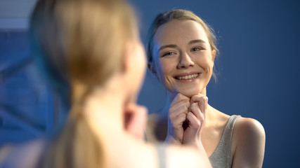 Adorable teenage girl smiling at mirror reflection, feeling cheerful and happy