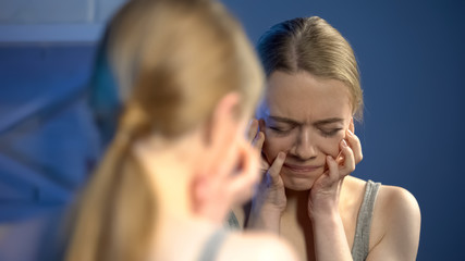 Deeply upset young woman looking sadly mirror, unhappy with appearance, puberty