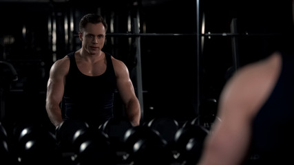 Fototapeta na wymiar Motivated bodybuilder looking in mirror reflection during break between workouts