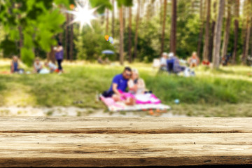 Table background with wooden top board with nice forest and gardens view in distance. Happy barbecue or picnic time with family. Empty space on the table top for an advertising product..