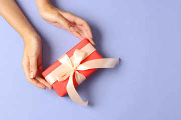 gift in female hands on a colored background top view.