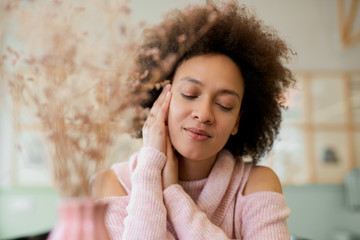 Portrait of charming mixed race woman in pink turtleneck sweater sitting in cafe.