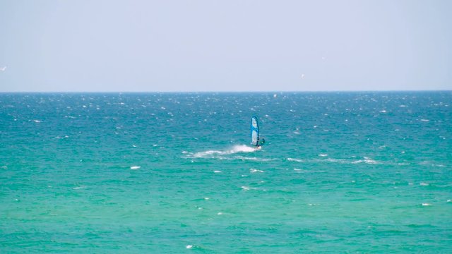 Windsurfer riding the waves in the sea. Shot. Windsurfer in the sea, man on windsurf conquering the waves, enjoying extreme sport, active lifestyle, happy summer vacation