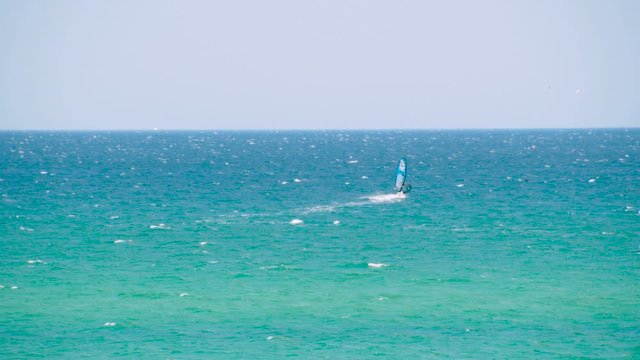 Windsurfer riding the waves in the sea. Shot. Windsurfer in the sea, man on windsurf conquering the waves, enjoying extreme sport, active lifestyle, happy summer vacation