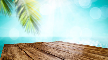 Wooden table top backround with beautiful calm ocean in distance. Some palm leaves above the wooden top board. Empty space for an advertising product.