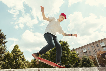 Skateboarder doing a trick at the city's street in sunny day. Young man in sneakers and cap riding...