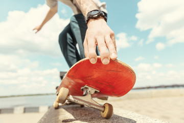 Skateboarder doing a trick at the city's street in sunny day. Young man in sneakers and cap riding...