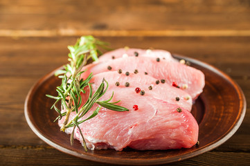 Meat fillet in a plate with rosemary, peppercorns close-up. Chicken, turkey, pork, beef fillet in a plate on a textured wooden table, copy space.