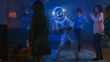 At the College House Costume Party: Fun Guy Wearing Space Suit Dances Off, Doing Robot Dance Modern Moves. With Him Beautiful Girls and Boys Dancing in Neon Lights. © Gorodenkoff