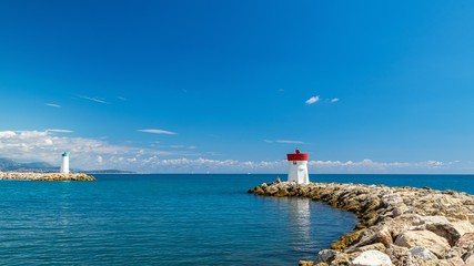 Fototapeta na wymiar wo lighthouses at the entrance to the Bay of the French Riviera on a clear Sunny day against a blue sky with clouds with a rocky shore