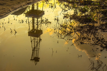 Reflection of blurred image of an oil rig in a puddle of oil. Dead plants. The concept of...