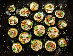 Small pizzas with zucchini with the addition of brown mushrooms, mushroom chanterelles, mozzarella cheese and fresh parsley on a black background, top view, close up. Vegetarian food