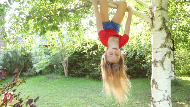 Happy little girl hanging from a tree playing in a sunny backyard summer fun concept_9795