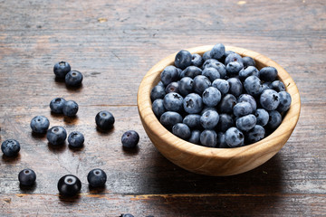 Freshly picked blueberries in wooden bowl on wooden background.