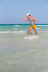 Fototapeta premium A young man stands in the sea, holds his hat and looks aside. Horizontally.