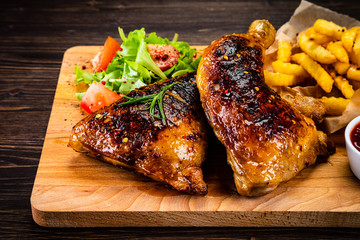 Roasted chicken leg with french fries and vegetable salad on wooden background