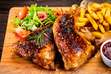 Roasted chicken leg with french fries and vegetable salad on wooden background