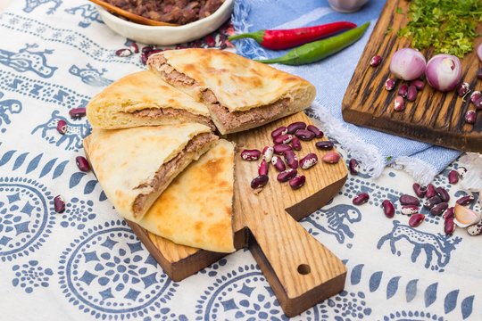 Lobiani pie - Georgian cuisine traditional food stuffed with red kidney or white beans (lobio) inside on wooden board and Lurji Supra tablecloth.