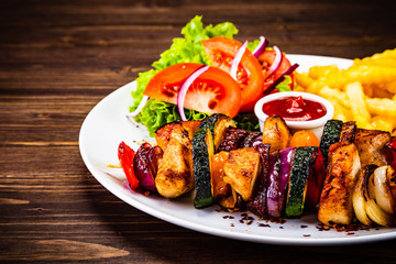 Kebabs - grilled meat with french fries and vegetables on wooden background